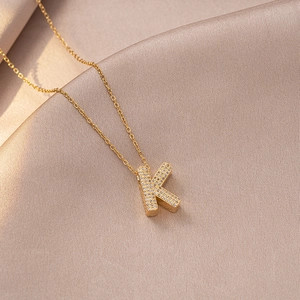 Macro shot of gold letter K pendant with sparkling zircon on champagne silk background