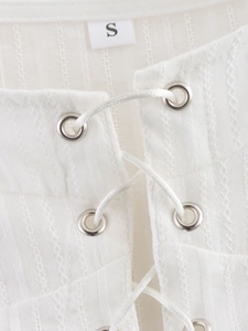 Detail of white textured fabric top featuring metal eyelets and intricate lace-up design