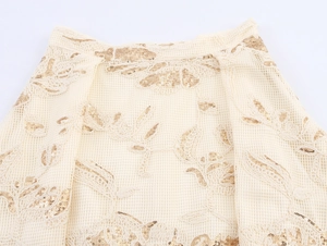 Detail of mesh fabric with golden sequins and floral embroidery on an elegant beige skirt