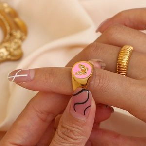 Detail of gold butterfly ring with pink enamel and sparkling zircon stones on finger