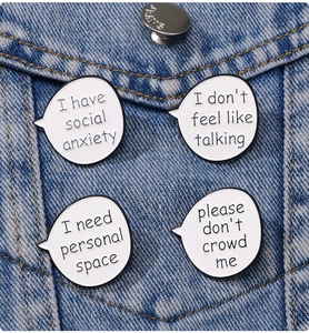Detail of four white enamel quote pins on denim jacket showing social anxiety phrases