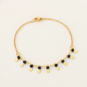 Detail of gold chain bracelet featuring faceted black beads and teardrop charms