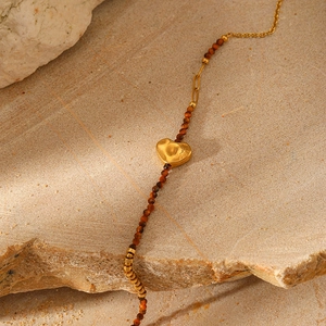 Macro shot of gold irregular heart pendant with reddish-brown garnet beads on beige stone
