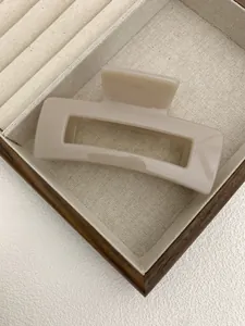 Macro detail of a large cream square hollow hair claw clip on a luxury jewelry tray