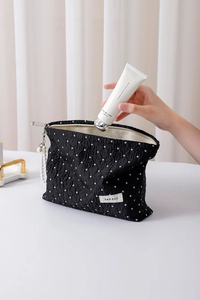 Detailed shot of black polka dot pouch with pearl zipper and hand placing cream inside