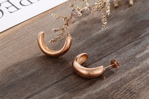 Detail showing polished rose gold C-shaped hoop earrings on a rustic wooden background