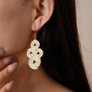 Close-up of layered golden textured hoop earrings with a spiral weave pattern on a model