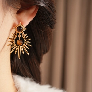 Close-up of gold starburst earrings with brown stones and sparkling zirconias on ear