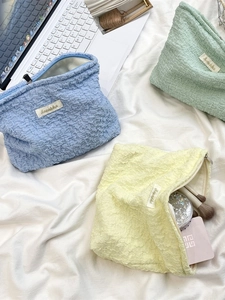 Textured bubble fabric cosmetic bags in blue, green, and yellow on a white cloth background