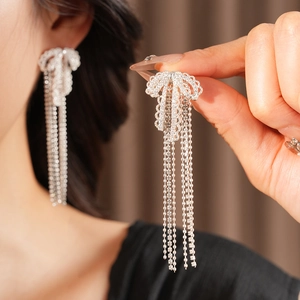 Macro detail of silver bow earrings with sparkling rhinestone tassels and elegant design