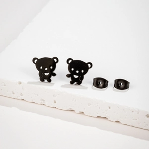 Close-up of matte black teddy bear stud earrings with hollow design on white stone surface