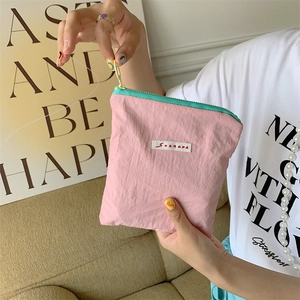 Pink nylon pouch with green zipper held by hand, featuring SOZAKKA brand woven label