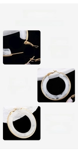 Detail view of large gold hoop earrings with white marble resin inlay and polished finish