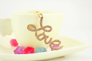 Close-up of golden metal Love keychain with inlaid rhinestones on a white ceramic cup