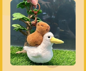 Close-up of a plush capybara riding a white duck with a metal keychain and bell