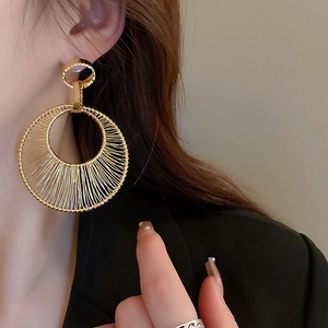 Close-up of model wearing gold woven wire hollow hoop earrings with intricate metal craftsmanship