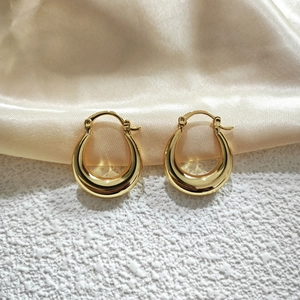 Close-up of golden U-shaped hollow earrings on champagne silk fabric background