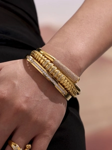 Close-up of stacked gold-plated bangles with clear and purple zircon stones on a model