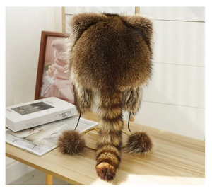 Detail of faux raccoon fur hat with striped tail and plush pom-poms on a gold stand