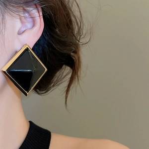 Détail de boucles d'oreilles vintage en résine noire avec bordure dorée sur un modèle
