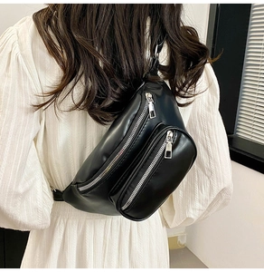 Detail of black PU leather chest bag with dual zippers and stylish chain on a white dress