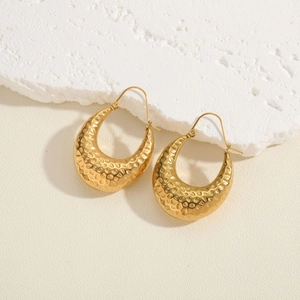 Macro view of gold hammered texture hoop earrings on a white marble surface