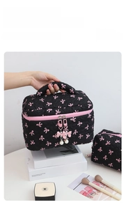 Detail of a black quilted makeup bag with pink bow patterns and a pearl zipper charm