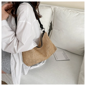 Detail of hand-woven straw hobo bag with black leather strap and metal ring hardware