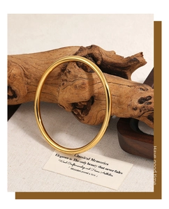 Detailed view of a 4mm polished gold bangle on a rustic textured linen background