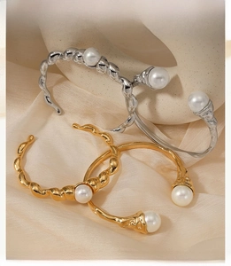 Close-up of twisted stainless steel bangles in gold and silver with pearl detail