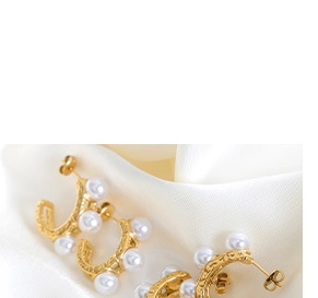 Détail de boucles d'oreilles créoles dorées avec texture et perles blanches