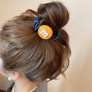 Détail d'un chouchou bleu en tissu avec pendentif lettre M orange sur queue de cheval