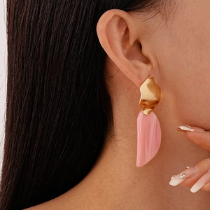 Détail de boucles d'oreilles en acrylique rose avec pièces dorées irrégulières sur un mannequin