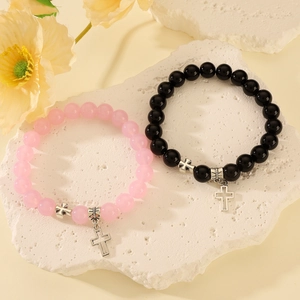 Vista detallada de pulseras elásticas de cuentas con cruz en rosa y negro sobre piedra