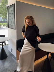 Detail eines schwarzen Oversize T-Shirts kombiniert mit weißem Satinrock in einem Café
