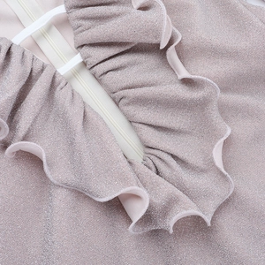 Close-up of champagne pink glitter fabric featuring ruffle trim and white hidden zipper