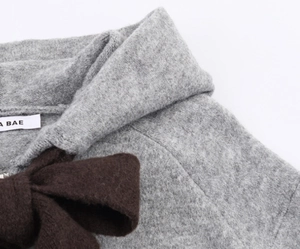 Close-up of a large brown knit bow detail on a grey sweater with the A BAE neck label