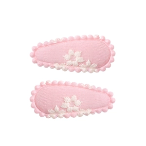 Detail of pink fabric-wrapped hair clips with white flower embroidery and wavy lace edges