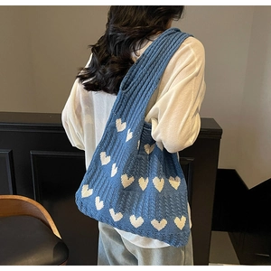 Detalle de bolso de hombro de punto azul con patrones de corazones blancos en la modelo