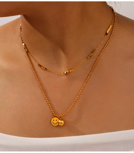 Detail of layered gold titanium necklace featuring a smiley face pendant and geometric beads