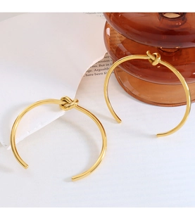 Detail of golden knot open earrings with metallic luster on elegant white minimalist background