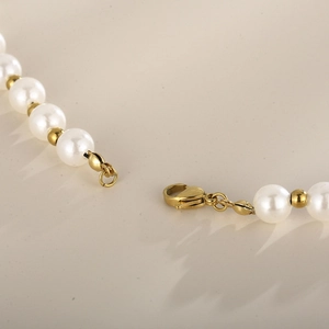 Vue macro du fermoir mousqueton doré sur un collier de perles blanches et billes dorées