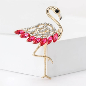 Elegant gold flamingo brooch with white rhinestones and red teardrop gems on a white block