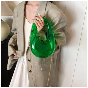 Close-up of a green transparent acrylic evening bag with gold chain and U-shaped handle