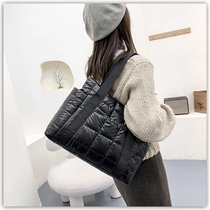 Detail of a large black quilted tote bag with glossy finish and durable nylon straps
