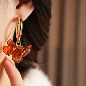 Close-up of model wearing C-shaped gold hoop earring with amber resin flower petal charm