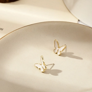 Macro shot of gold and white butterfly stud earrings resting on a ceramic tray