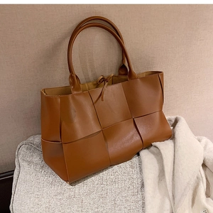 Close-up of brown woven leather tote bag texture on a neutral textured cushion