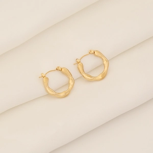 Macro shot of gold hoop earrings with irregular wave texture on white silk background
