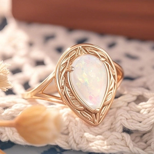 Makroaufnahme eines Vintage-Opalrings mit goldenen Ranken auf weißer Spitze